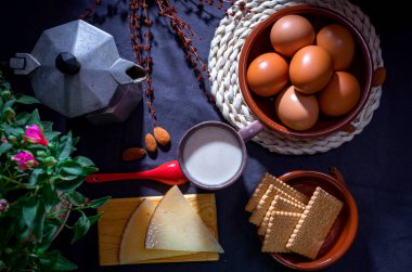 Eggs, cheese, cookies and coffee served for breakfast on a dark background with a fuchsia flower in the background.