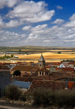 An old Spanish village among the golden fields of Castilla La Mancha on a sunny day with rich blue skies and white fluffy clouds