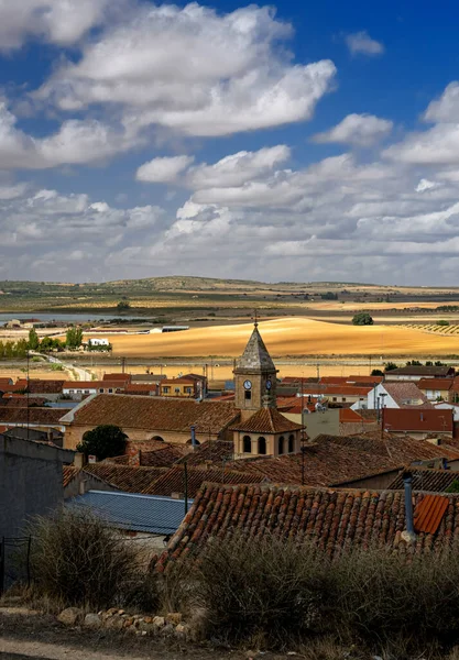 Eski bir İspanyol köyü Castilla La Mancha 'nın altın tarlalarının arasında güneşli bir günde zengin mavi gökyüzü ve beyaz kabarık bulutlarla