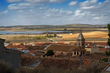 An old Spanish village among the golden fields of Castilla La Mancha on a sunny day with rich blue skies and white fluffy clouds