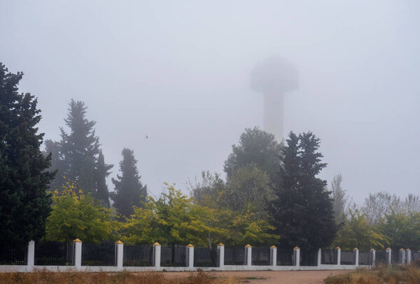 Autumn city park on a foggy morning with a water tower in the background.