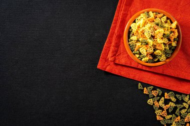 Multicolored pasta in the form of dinosaurs on a red napkin on a dark tablecloth