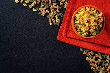 Multicolored pasta in the form of dinosaurs on a red napkin on a dark tablecloth