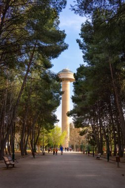 Uzun ağaçlı şehir parkı ve su kulesi olan sarı taş yollar.