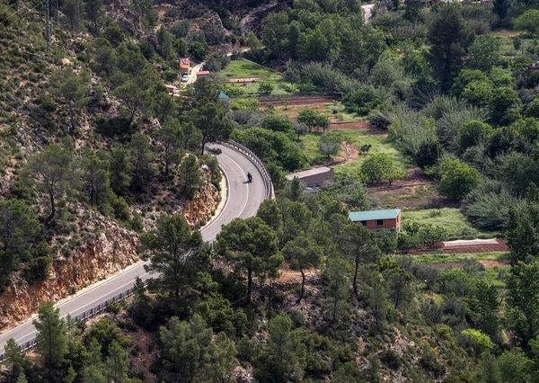 A motorcycle rides along a winding mountain road on a sunny day. View from above