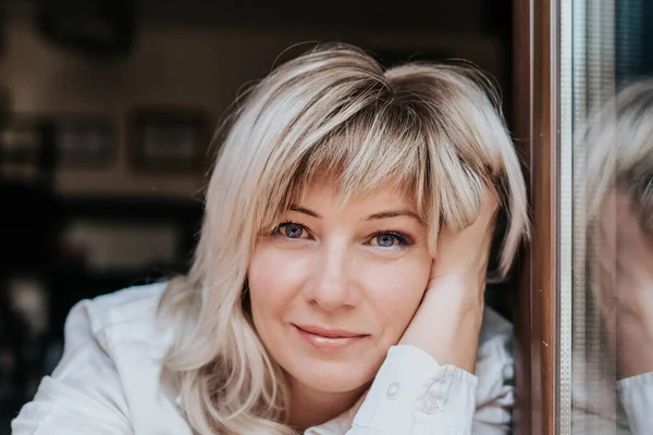 stock image Blonde woman in a white blouse sits leaning on her hands in natural light