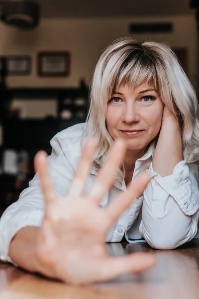 stock image Blonde woman in a white blouse sits leaning on her hands in natural light