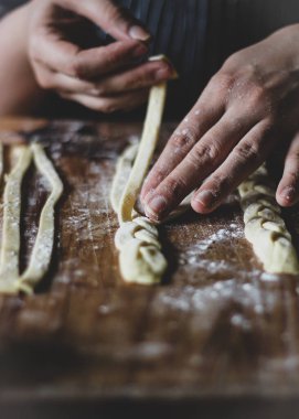 close-up of female hands hand braiding pie dough with flour on a wooden surface