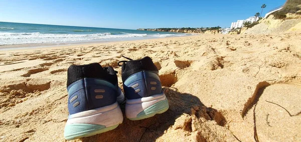 Blue tennis shoes on the sand by the sea
