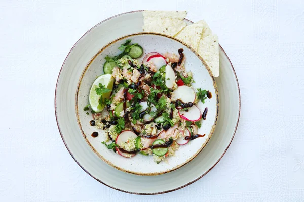 Renkli ve taze sebze salatası ve kinoalı büyük kâse manzarası. Nachos 'lu tabak. Masa olarak beyaz arkaplan.