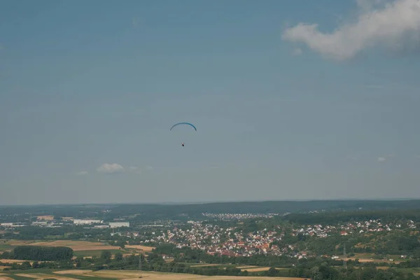 Cesur bir paraglider, resim gibi Alman kırsalında yükseliyor. Arka planda tuhaf bir kasaba var..