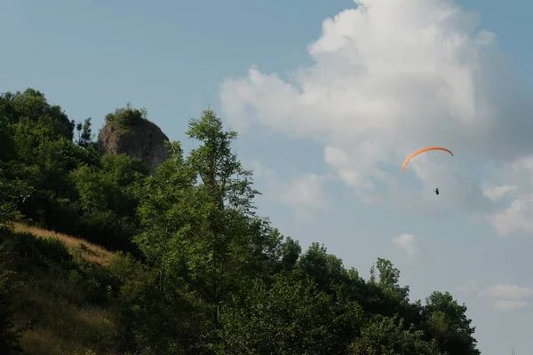 Korkusuz bir paraglider tepelik bir arazide süzülüyor, güneş ışığıyla yıkanmış ve canlı yeşilliklerle dolup taşıyor..