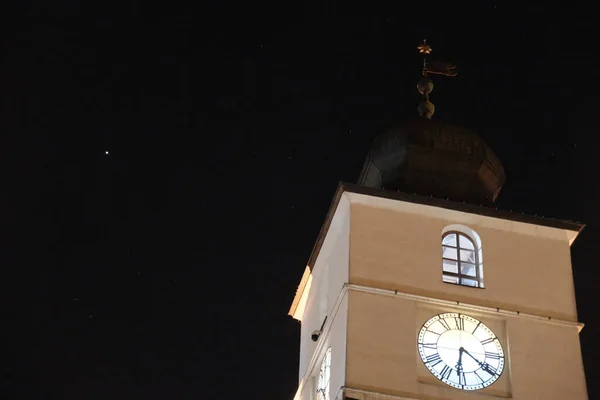 Karanlık gökyüzüne karşı aydınlanan ve ihtişamını ve tarihsel mimarisini yeni bir ışıkta sergileyen bir Romen saat kulesinin çarpıcı gece manzarası.