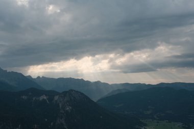 Bavyera dağlarının çarpıcı panoramik bir görüntüsü dramatik bulutlu bir gökyüzü altında, bu Alp manzarasının görkemli ve ehlileştirilmemiş güzelliğini kapsıyor..