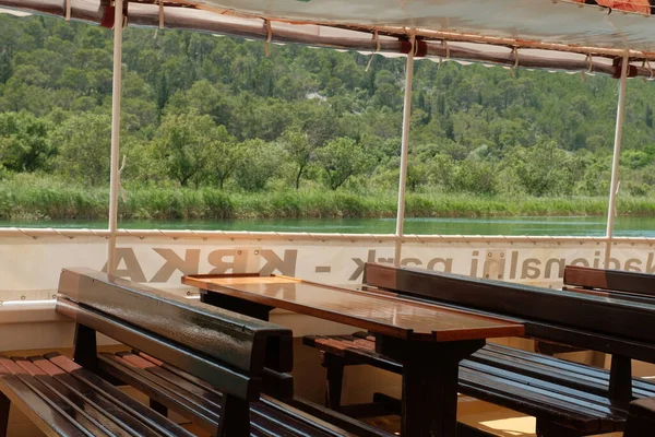 Bir feribotun içinde, su yolculuğunun ortasında kırsal bir cazibeyi vurgulayan, ahşap bankların ve bir masanın basit rahatlığını gösteren bir feribot..