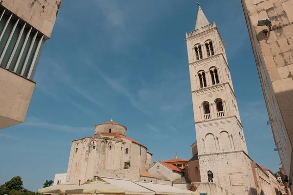 Zadar 'da güneşli bir günün canlı bir görüntüsü, tarihi kilise ve saat kulesinin mimari uyumunu gösteriyor, bu Hırvat kentinin imzalı simgeleri..