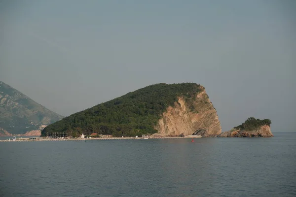 Karadağ 'ın Budva kenti yakınlarındaki masmavi sulardan, verimli yeşilliklerle bezenmiş nefes kesici, üçgen şekilli bir kaya adası zarif bir şekilde ortaya çıkıyor..