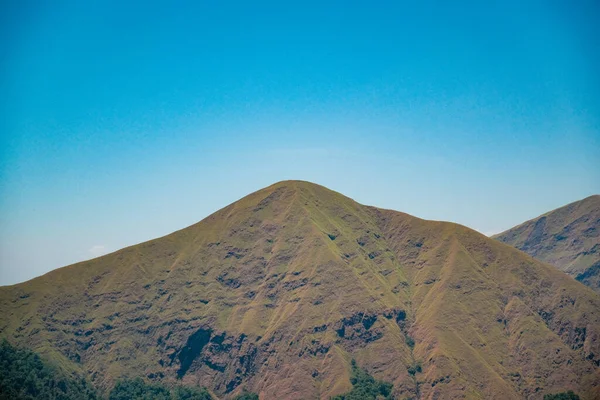 From this serene vantage point, capture the essence of one of Pergasingan\'s enchanting hills against the backdrop of a flawless, clear blue sky.