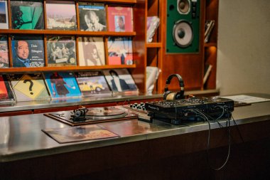 Arka planda eski plaklarla süslenmiş bir kahve dükkanının nostaljik cazibesine kapıl. Masasında kulaklık olan klasik bir plak çalar rahat bir atmosfer yaratır.