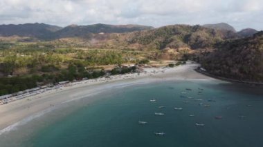 İnsansız hava aracı sahile doğru giderken Lombok 'un kıyı güzelliğinin canlı duvar halısını yakalayın. Geleneksel balıkçı teknelerinden hevesli sörfçülere ve sahil tesislerine