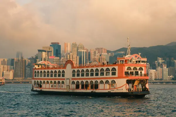 Daha yakından bakınca, eski usul turuncu bir feribotun, Hong Kong 'un hareketli limanında, şehrin klasik cazibesiyle harmanlanmış bir şekilde yüzdüğünü görüyoruz.