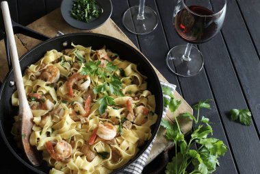 Italian Traditional Dish tagliatelle pasta with shrimp and mushrooms and  garnished with fresh parsley on dark background.  Italian pasta. Directly above.