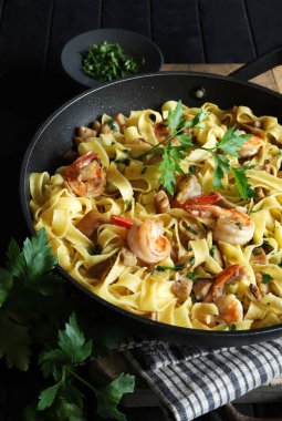 Italian Traditional Dish tagliatelle pasta with shrimp and mushrooms and  garnished with fresh parsley on dark background.  Italian pasta. Directly above.