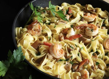 Italian Traditional Dish tagliatelle pasta with shrimp and mushrooms and  garnished with fresh parsley on dark background.  Italian pasta. Directly above.