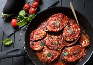 A pan with slices of eggplant with tomato sauce, parmesan cheese and basil on dark background. Directly above.