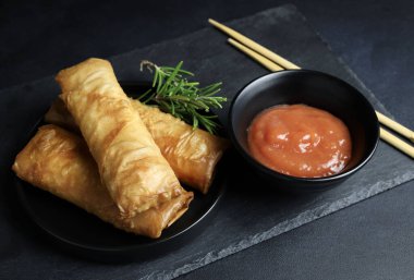 Fried spring rolls with sweet chili sauce on a dark background. Asian cuisine.
