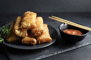 Fried spring rolls with sweet chili sauce on a dark background. Asian cuisine.
