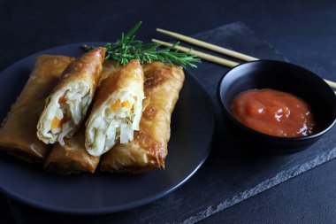 Fried spring rolls with sweet chili sauce on a dark background. Asian cuisine.