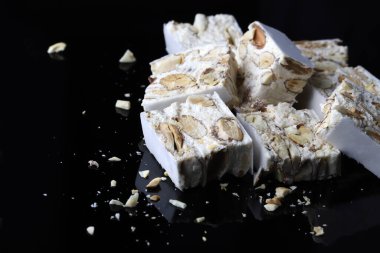 Torrone - soft Italian nougat with almonds isolated on black background. Holiday season. Copy space.