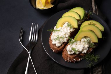 Healthy appetizer with cereal bread, avocado and soft cheese on dark background. Directly above. Copy space.
