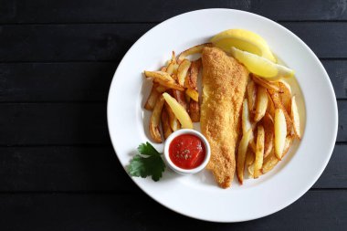 Traditional British fish and chips in white plate on wooden background. Directly above.