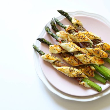 Concept of homemade appetizer. Asparagus wrapped in prosciutto and puff pastry, decorated with poppies seeds on white background. Directly above.
