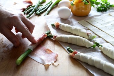 Prosciutto ve ahşap masaya puf böreği sarılmış kuşkonmaz hazırlıyorum. Lezzetli bahar aperatifleri. Tam üstte.