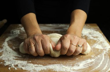 Geleneksel ev yapımı makarna hamuru hazırlıyorum. Un kaplı bir masada ekmek ya da pizza yapmak için taze hamur yoğuran kadın ellerine yakından bakın. Karanlık arka plan. Boşluğu kopyala.