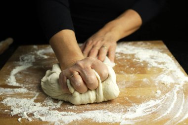 Geleneksel ev yapımı makarna hamuru hazırlıyorum. Un kaplı bir masada ekmek ya da pizza yapmak için taze hamur yoğuran kadın ellerine yakından bakın. Karanlık arka plan. Boşluğu kopyala.