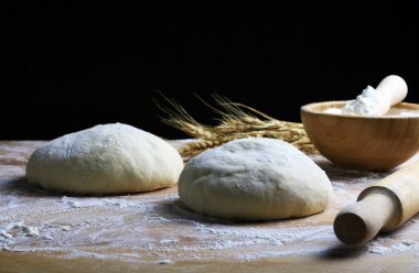 Pişirmeye hazır ev yapımı makarna hamuru ve un ahşap bir masada buğday kulağı. Siyah arka plan. Boşluğu kopyala.