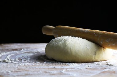 Ev yapımı taze makarna hamuru un kaplı ahşap bir masada merdaneyle pişirilmeye hazır. Siyah arka plan. Boşluğu kopyala.