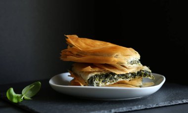 Ev yapımı Yunan yemekleri. Spanakopita, siyah arka planda ıspanaklı ve beyaz peynirli fillo hamur işi üçgeni. Uzayı kopyala Yakın plan..