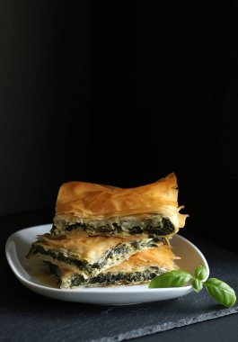 Ev yapımı Yunan yemekleri. Spanakopita, siyah arka planda ıspanaklı ve beyaz peynirli fillo hamur işi üçgeni. Uzayı kopyala Yakın plan..