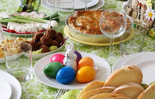 Easter holiday. Easter table decoration. Easter eggs, spring flowers and bunny decor. Bread, cheese, spinach pie, meat ball, vegetables.