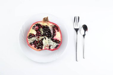 Beyaz arka planda izole edilmiş beyaz bir tabakta olgun nar kesiği. Tam üstte.