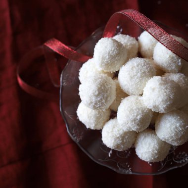 Ev yapımı yuvarlak hindistan cevizi ve beyaz çikolatadan yapılmış cam tabakta kırmızı arka planda. Raffaello şekeri. Noel süsü. Uzayı kopyala Tam üstte.