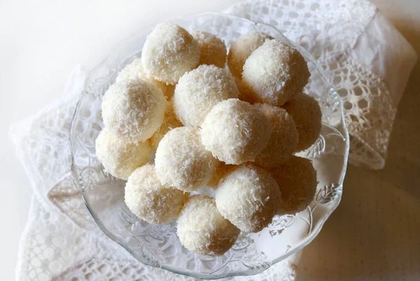Homemade round candies made of coconut and white chocolate in a glass dish on white background. Raffaello candy.  Copy space. Directly above.