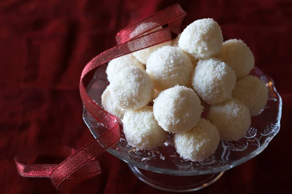 Homemade round candies made of coconut and white chocolate in a glass dish on red background. Raffaello candy. Christmas decoration. Copy space. Directly above.