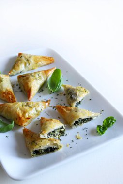 Geleneksel Yunan mutfağı. Spanakopita, ıspanaklı gevrek fillo hamur işi üçgeni, beyaz arka planda beyaz peynir. Tam üstte. Boşluğu kopyala.