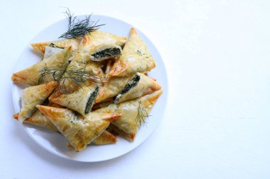 Geleneksel Yunan mutfağı. Spanakopita, ıspanaklı gevrek fillo hamur işi üçgeni, beyaz arka planda beyaz peynir. Tam üstte. Boşluğu kopyala.